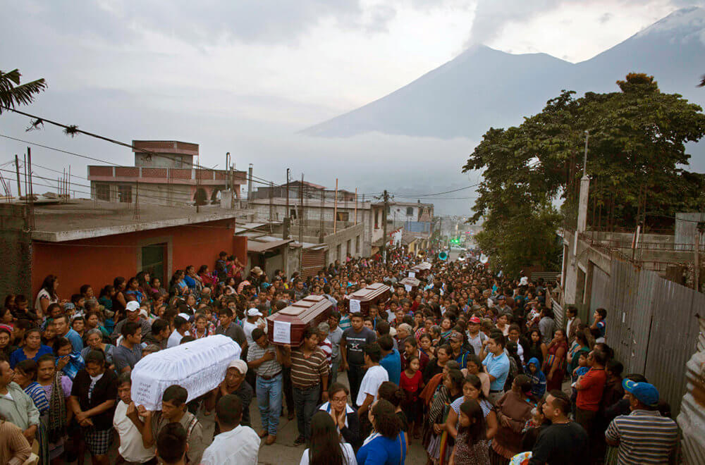 Mourners watch as caskets are carried through the street